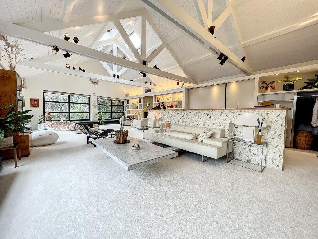 Salon contemporain lumineux avec plafond voûté, mobilier blanc minimaliste et décoration végétale.