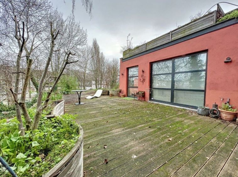 Terrasse moderne en bois avec mur rouge, mobilier relax, jardin et vue naturelle apaisante.