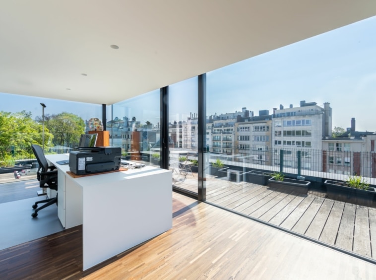 Bureau moderne avec vue urbaine, terrasse verte et mobilier contemporain pour productivité et détente.