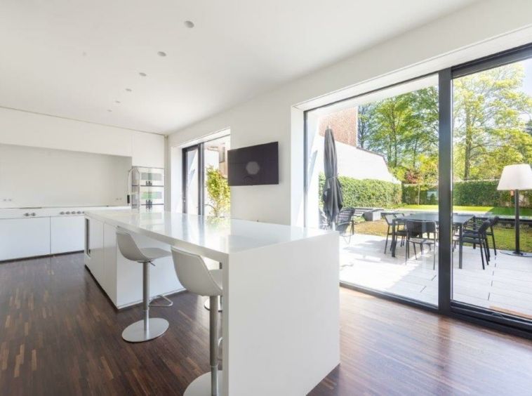 Cuisine moderne lumineuse avec espace extérieur, plan blanc, meubles intégrés, terrasse et ambiance chaleureuse.