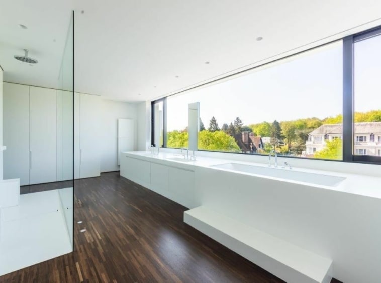 Salle de bain moderne lumineuse avec vue panoramique sur la nature, douche en verre et plan en blanc.