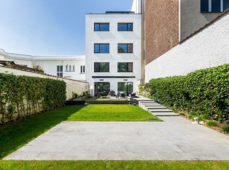 Villa moderne avec jardin lumineux, grande fenêtres, façade blanche et mur en brique à Bruxelles.