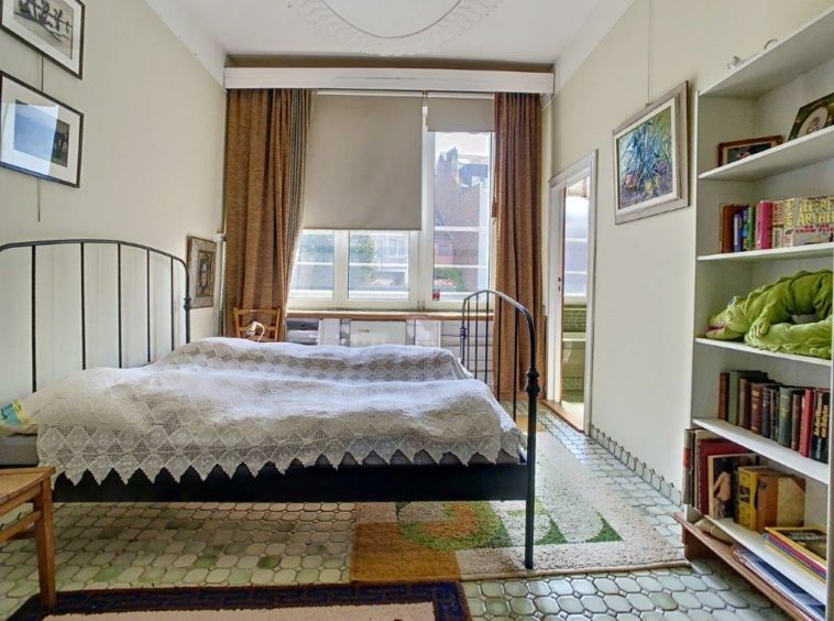 Chambre chaleureuse avec lit en fer, lumière naturelle, œuvres d’art, tapis coloré, ambiance cosy et inspirante.