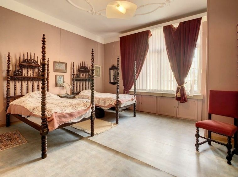 Chambre vintage chaleureuse avec lits à baldaquin, lumière naturelle et décor élégant en bois et tissus.