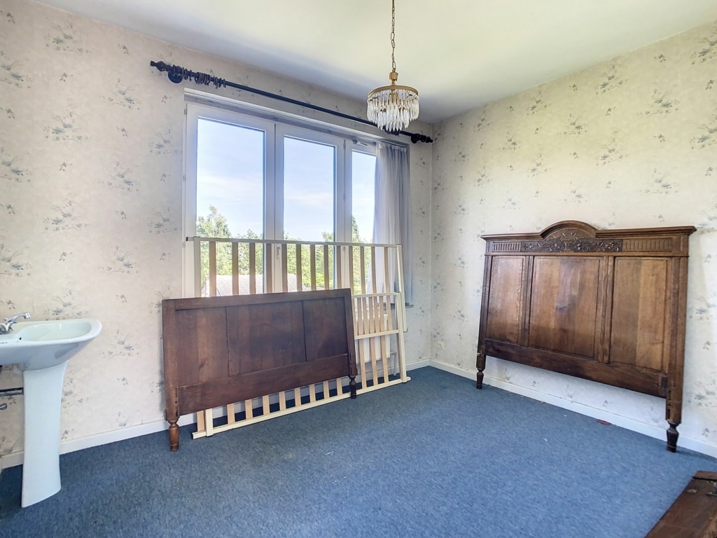 Chambre vintage lumineuse avec mobilier en bois, mur floral, lustre élégant et ambiance chaleureuse.