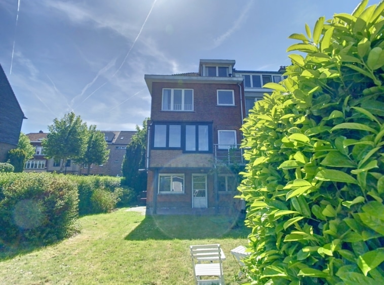 Maison en brique rouge avec jardin verdoyant et ciel bleu lumineux.