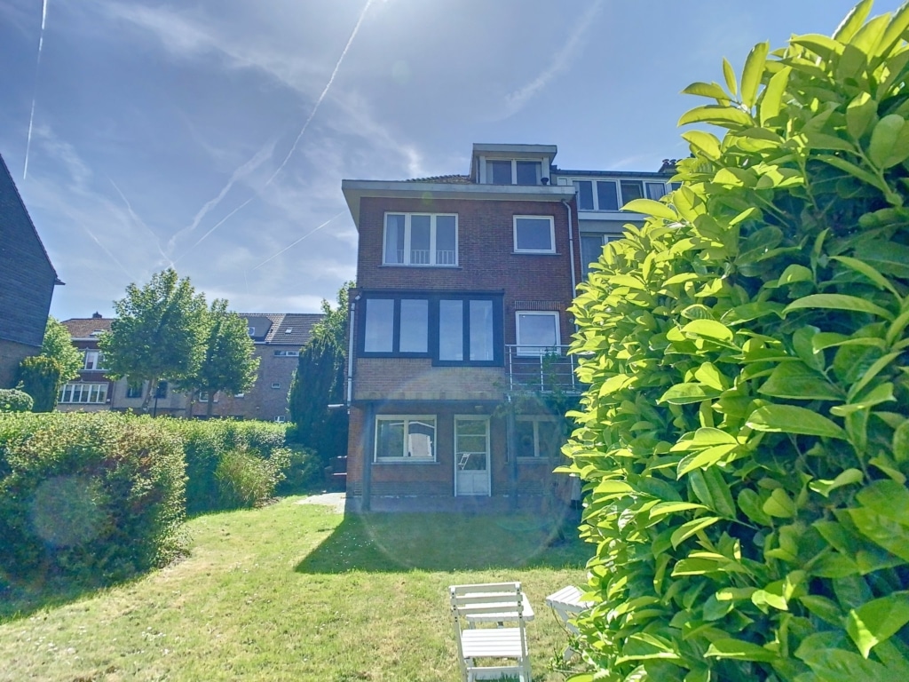 Maison en brique rouge avec jardin verdoyant et ciel bleu lumineux.