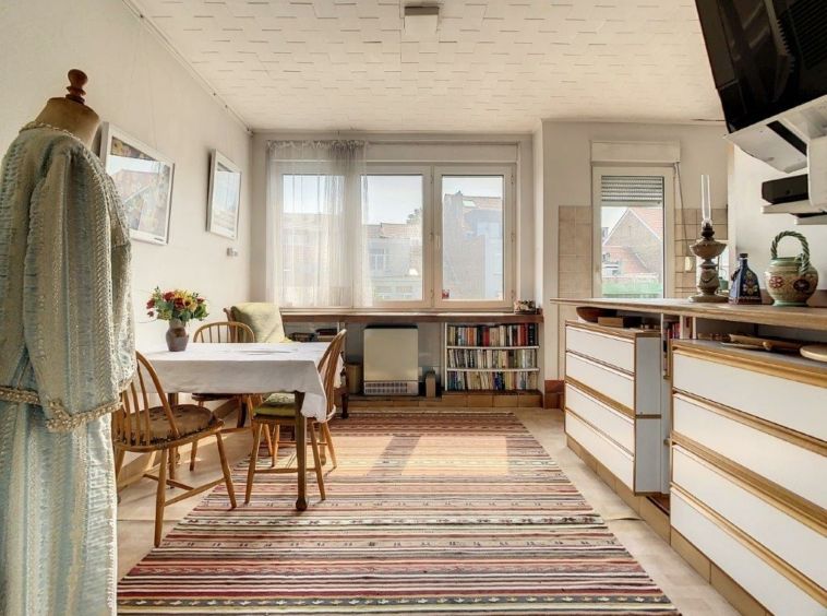 Salon cosy lumineux avec table en bois, étagère, mannequin créatif et tapis rayé.