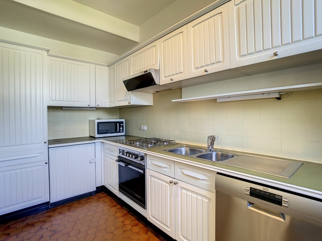 Cuisine moderne avec rangements blancs, appareils inox, plan clair et sol texturé chaud.