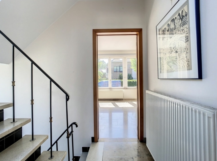 Escalier moderne lumineux menant à une pièce spacieuse avec grandes fenêtres et vue sur la nature.