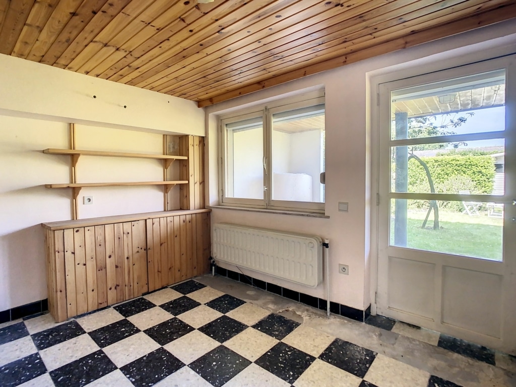Pièce lumineuse avec sol carreaux noir et blanc, fenêtres et étagère en bois clair.