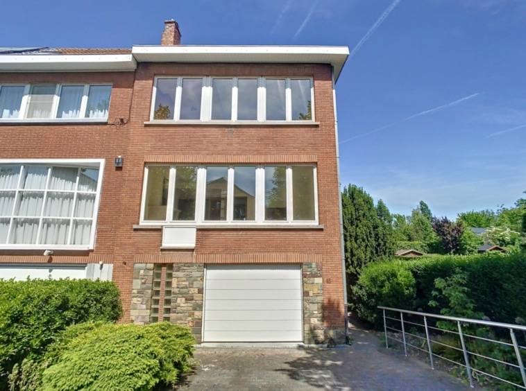 Maison familiale moderne en briques, jardin verdoyant, garage intégré, quartier paisible ensoleillé.