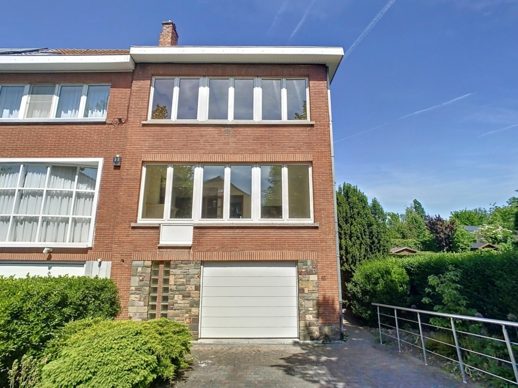 Maison familiale moderne en briques, jardin verdoyant, garage intégré, quartier paisible ensoleillé.