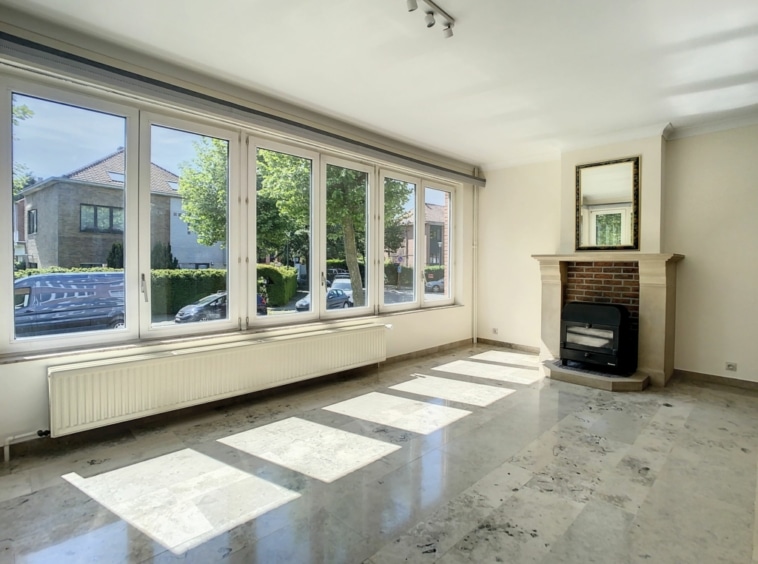 Salon lumineux avec cheminée moderne, grandes fenêtres, décor minimaliste et ambiance chaleureuse.