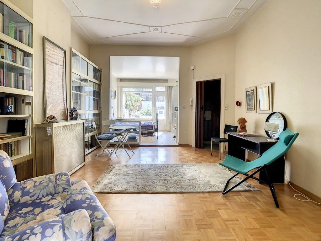 Salon lumineux avec espace de travail, canapé fleuri, tapis neutre, vue sur salle à manger.