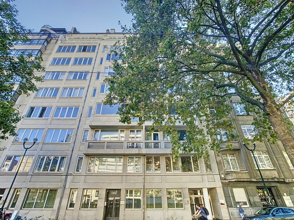 Appartement moderne avec grandes fenêtres, balcons, arbres luxuriants et ambiance urbaine sereine.