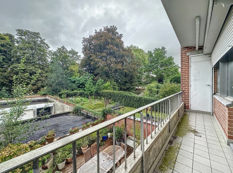 Balcon calme avec vue sur jardin luxuriant sous ciel gris, entouré de végétation verdoyante.
