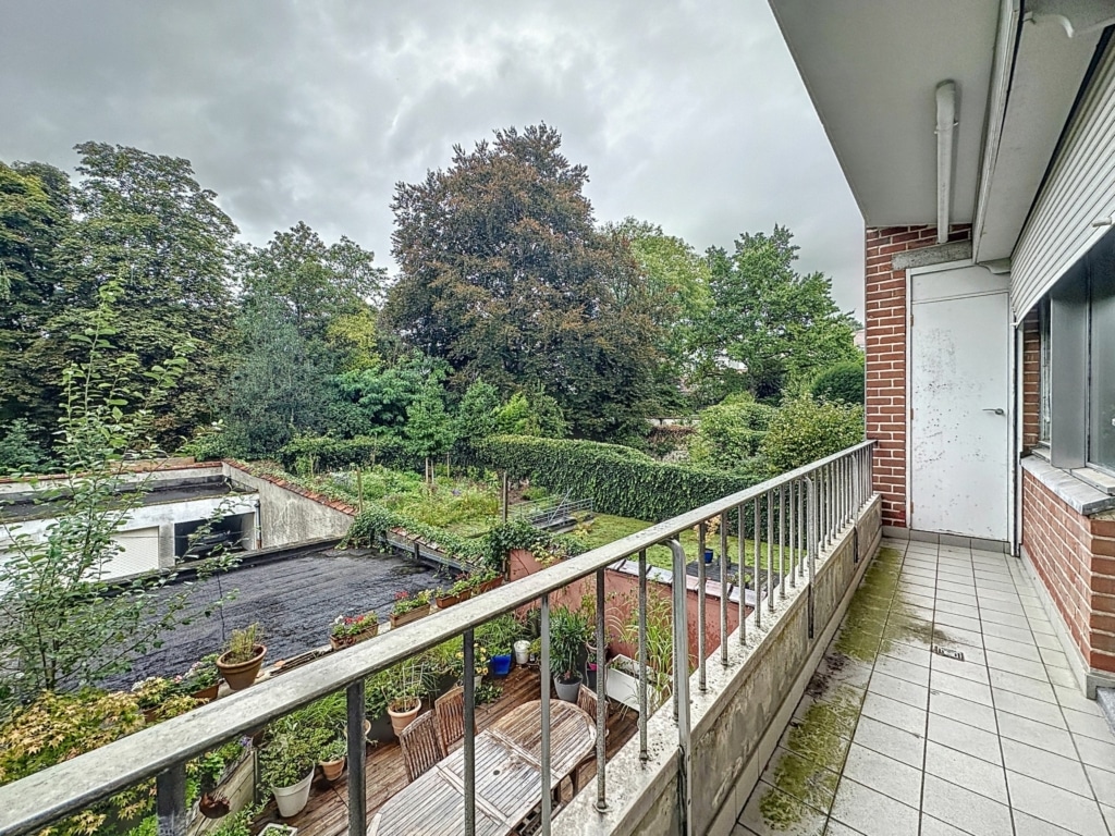 Balcon calme avec vue sur jardin luxuriant sous ciel gris, entouré de végétation verdoyante.