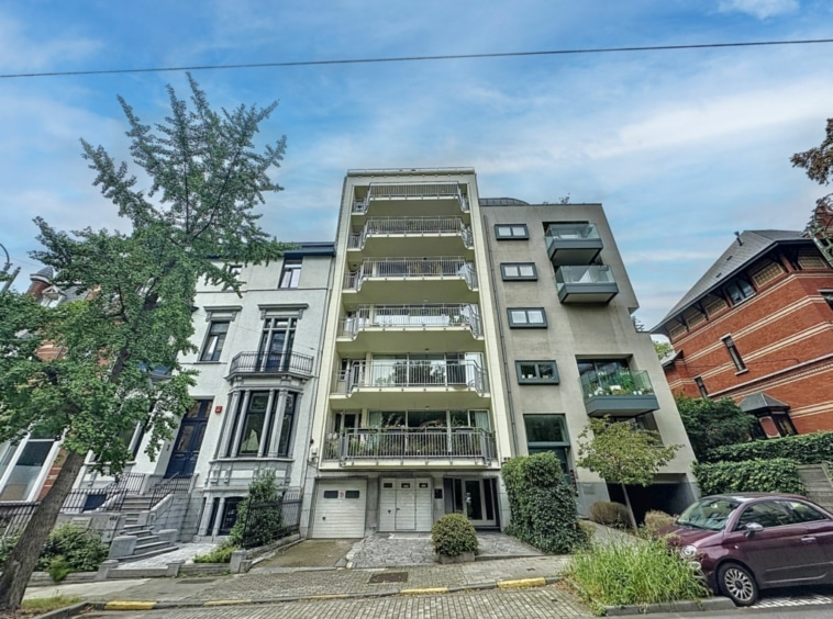 Adresse urbaine : immeuble moderne et résidence historique sous ciel bleu avec verdure et pavés.