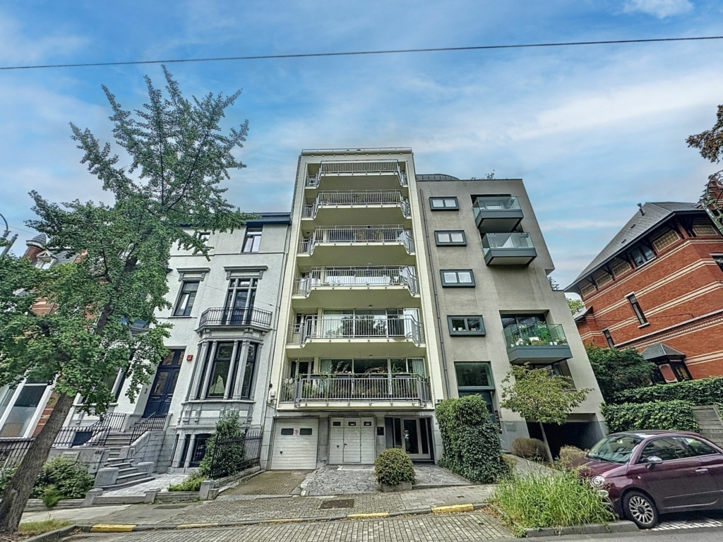 Adresse urbaine : immeuble moderne et résidence historique sous ciel bleu avec verdure et pavés.