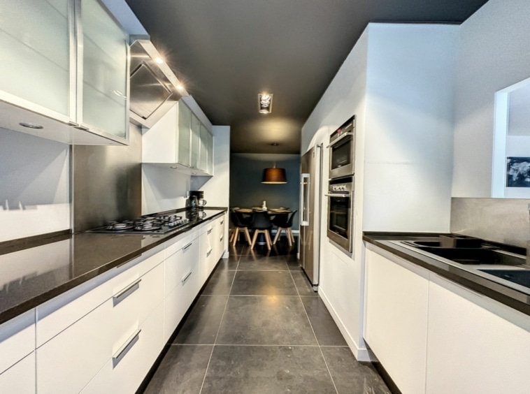Cuisine moderne blanche avec plan en pierre sombre, éclairage intégré et espace repas élégant.