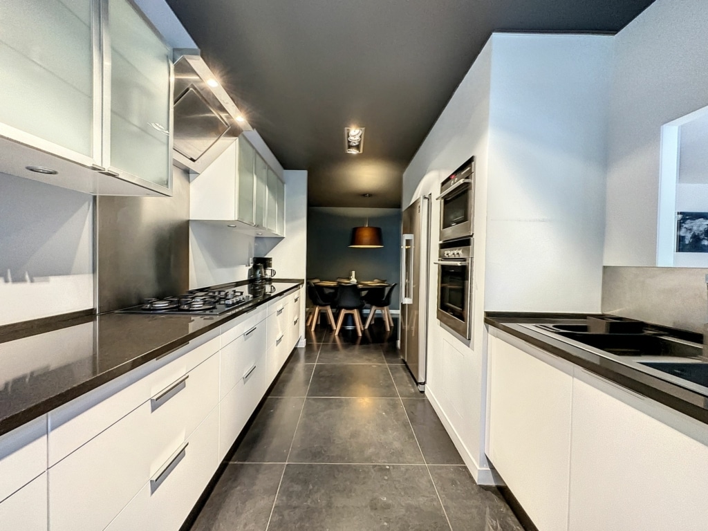 Cuisine moderne blanche avec plan en pierre sombre, éclairage intégré et espace repas élégant.