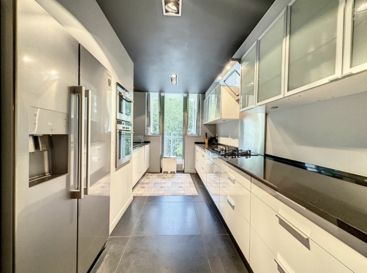 Cuisine moderne lumineuse avec meubles blancs, plan en quartz foncé et appareils intégrés élégants.