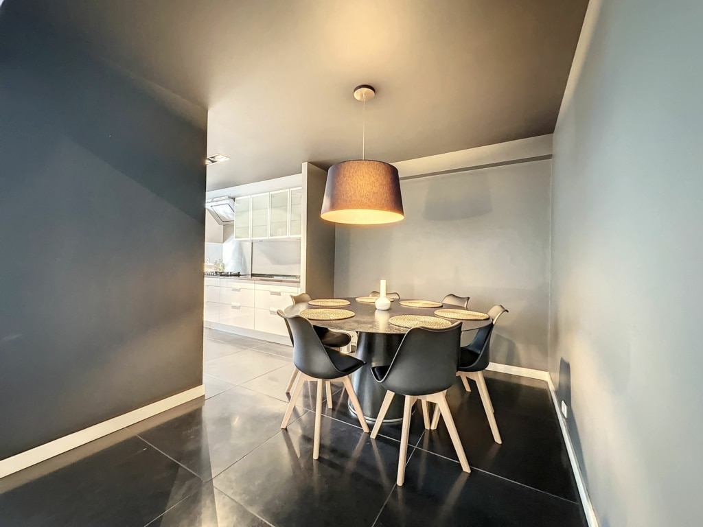 Salle à manger moderne avec table ronde, chaises ergonomiques, éclairage chaleureux, style épuré et élégant.