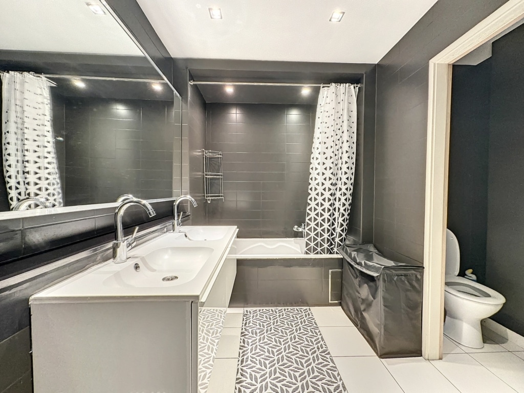 Salle de bain contemporaine élégante avec murs gris foncé, double lavabo, baignoire design, et éclairage chaleureux.