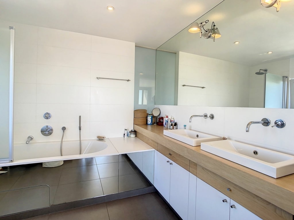 Salle de bain moderne avec double vasque, baignoire intégrée et éclairage naturel.