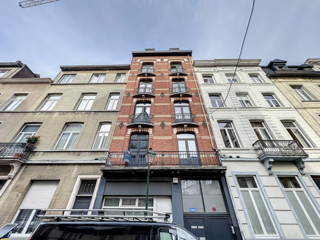 Bâtiment en briques rouges avec balcons en métal, fenêtres à volets, au cœur d’un quartier résidentiel.