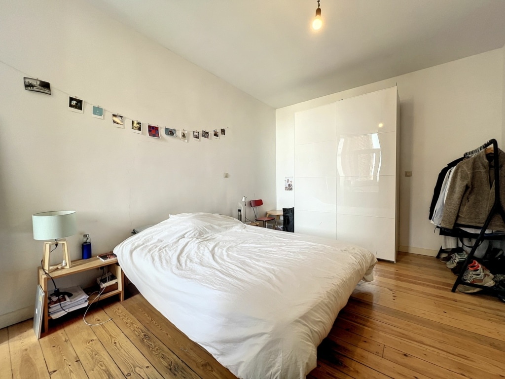 Chambre minimaliste lumineuse avec lit blanc, armoire brillante et décoration personnelle chaleureuse.