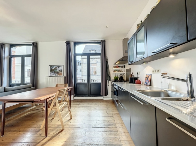Cuisine moderne lumineuse avec coin repas en bois, salon cosy et vue panoramique.