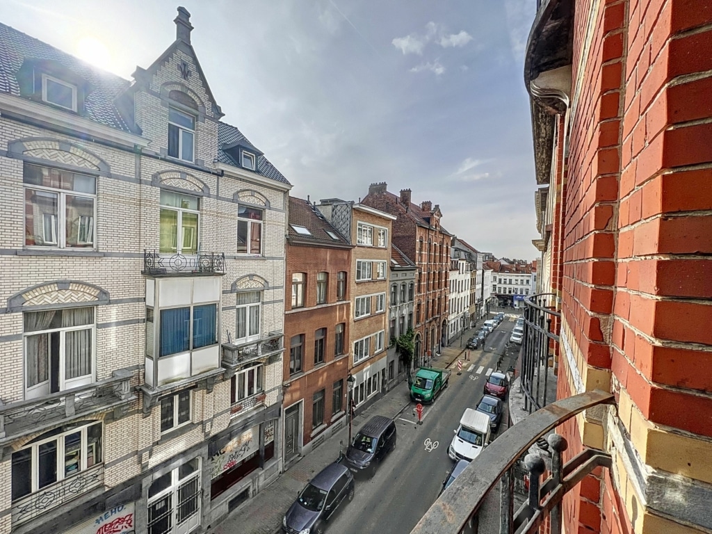 Rue animée avec bâtiments historiques, voitures colorées et ciel lumineux au cœur de la ville.