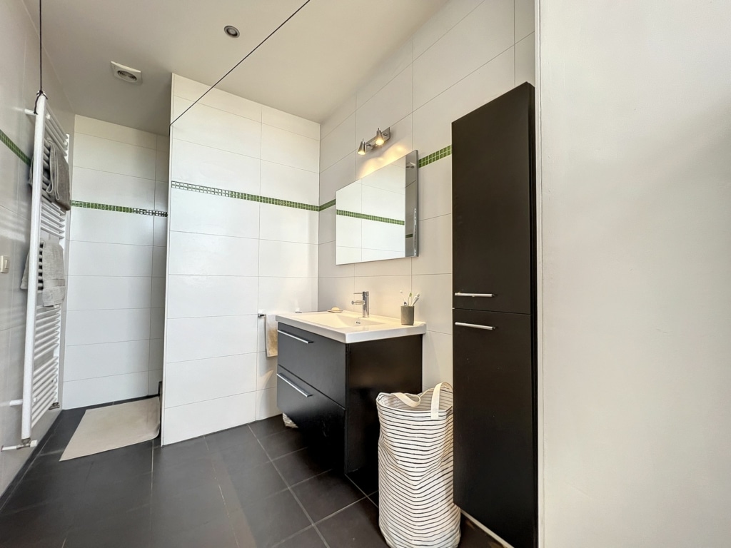 Salle de bain moderne épurée avec tuiles blanches, mobilier noir et accents verts.