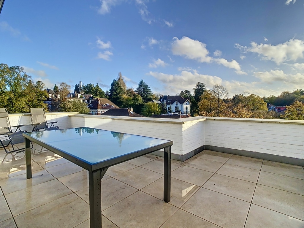 Balcon moderne avec vue automnale, mobilier en verre et métal sous un ciel bleu paisible.