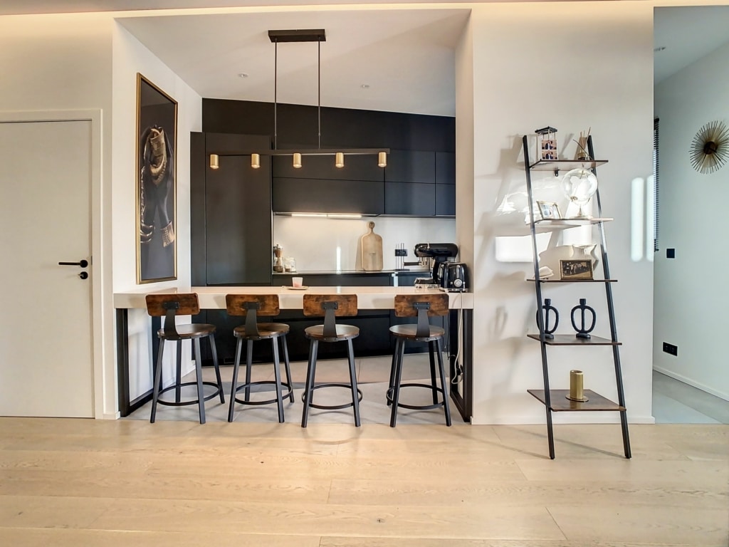 Cuisine moderne avec îlot blanc, mobilier en bois clair et armoires sombres élégantes.