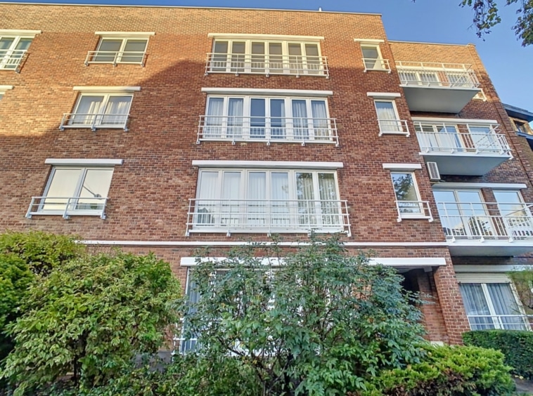 Immeuble résidentiel en briques avec balustrades, fenêtres variées, verdure, ambiance moderne et chaleureuse.