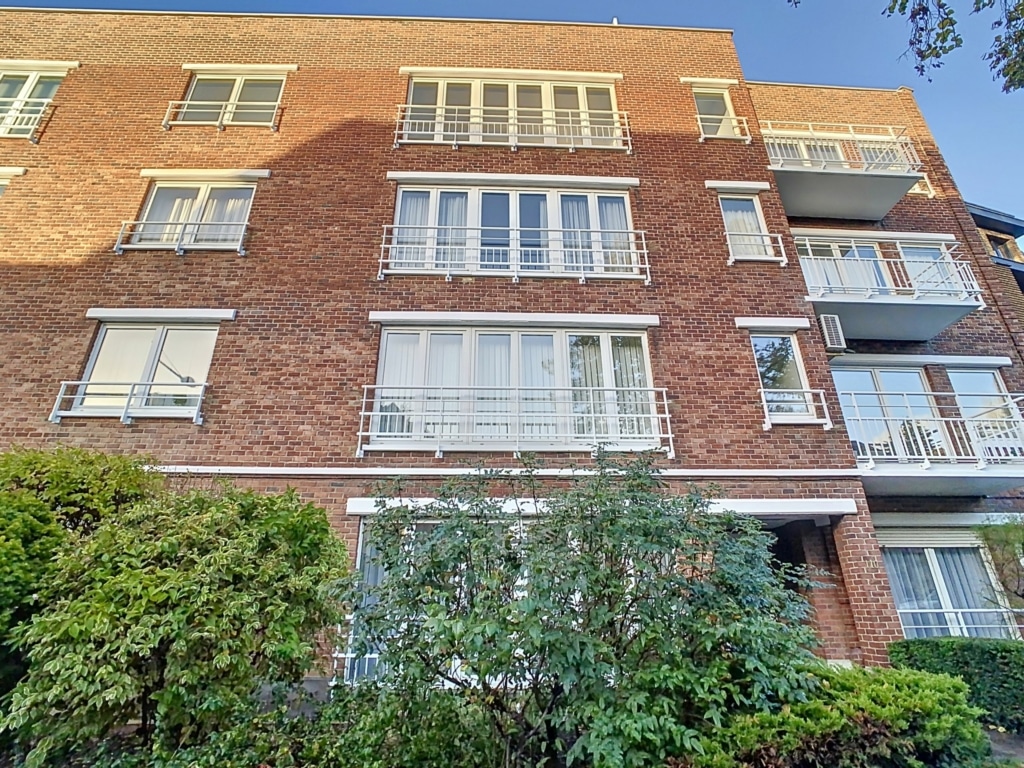 Immeuble résidentiel en briques avec balustrades, fenêtres variées, verdure, ambiance moderne et chaleureuse.