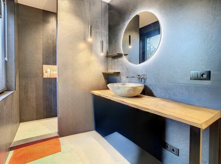 Salle de bain moderne avec miroir éclairé, plan en bois, lavabo en pierre et décoration élégante.