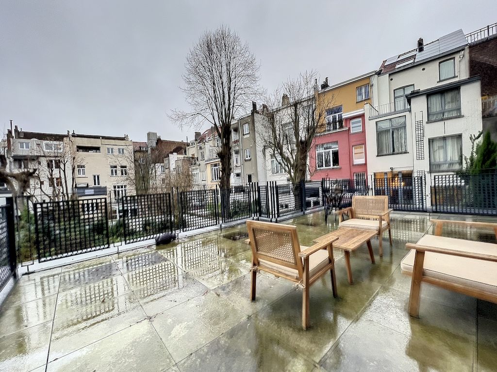 Balcon urbain paisible sous ciel gris avec des chaises en bois et bâtiments colorés en arrière-plan.