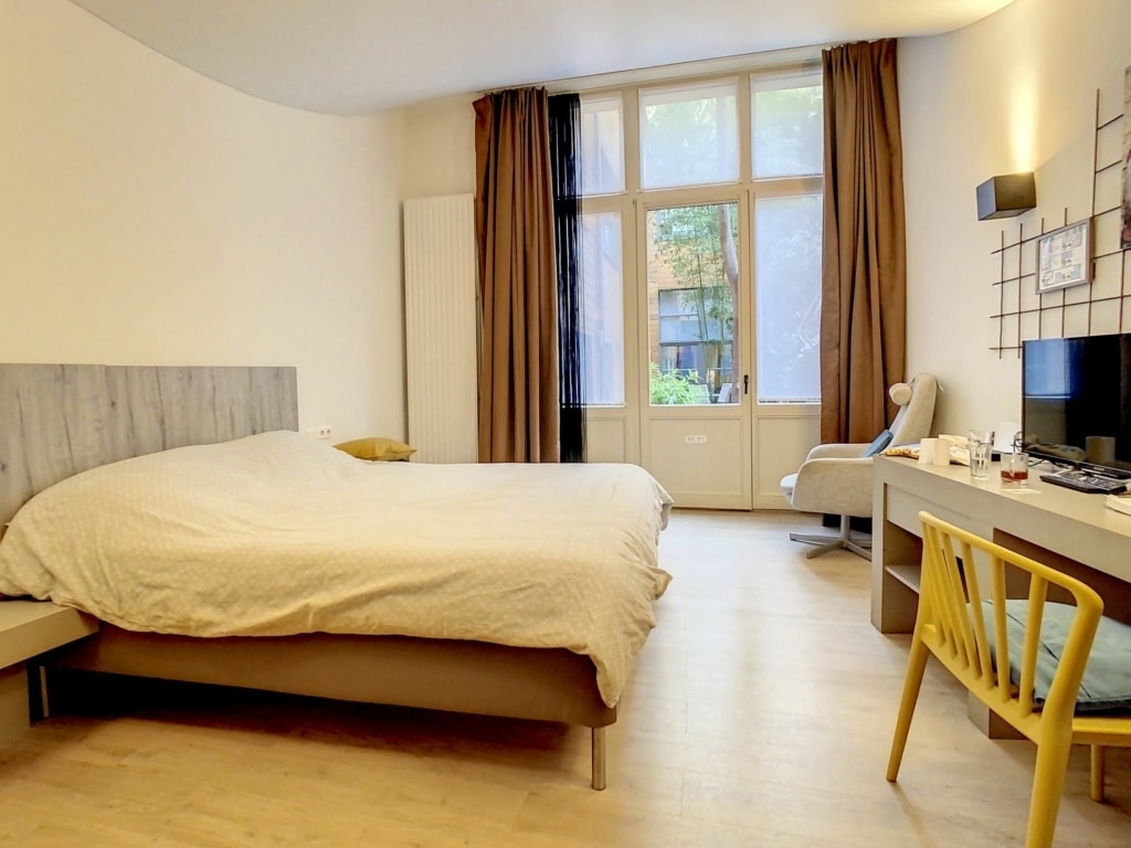 Chambre moderne et zen avec vue sur la nature, espace bureau, luminosité naturelle et ambiance relaxante.