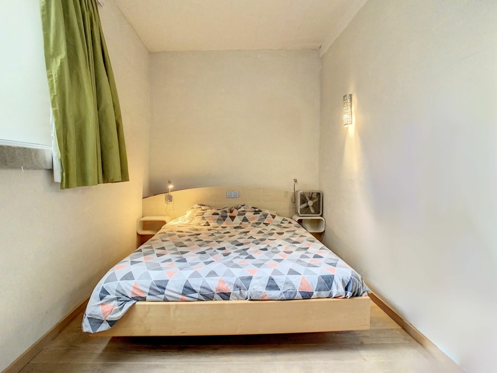 Chambre lumineuse et moderne avec lit en bois, décor géométrique et grande fenêtre vert pâle.