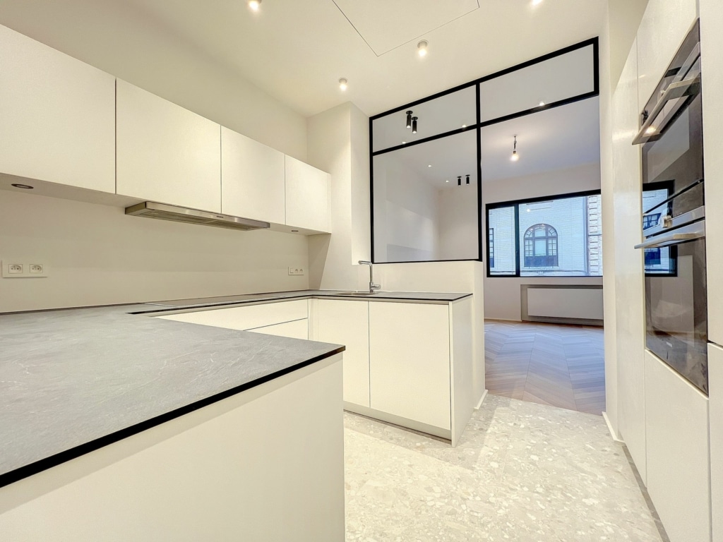 Cuisine moderne lumineuse avec mobilier blanc, éclairage naturel et plan de travail gris élégant.