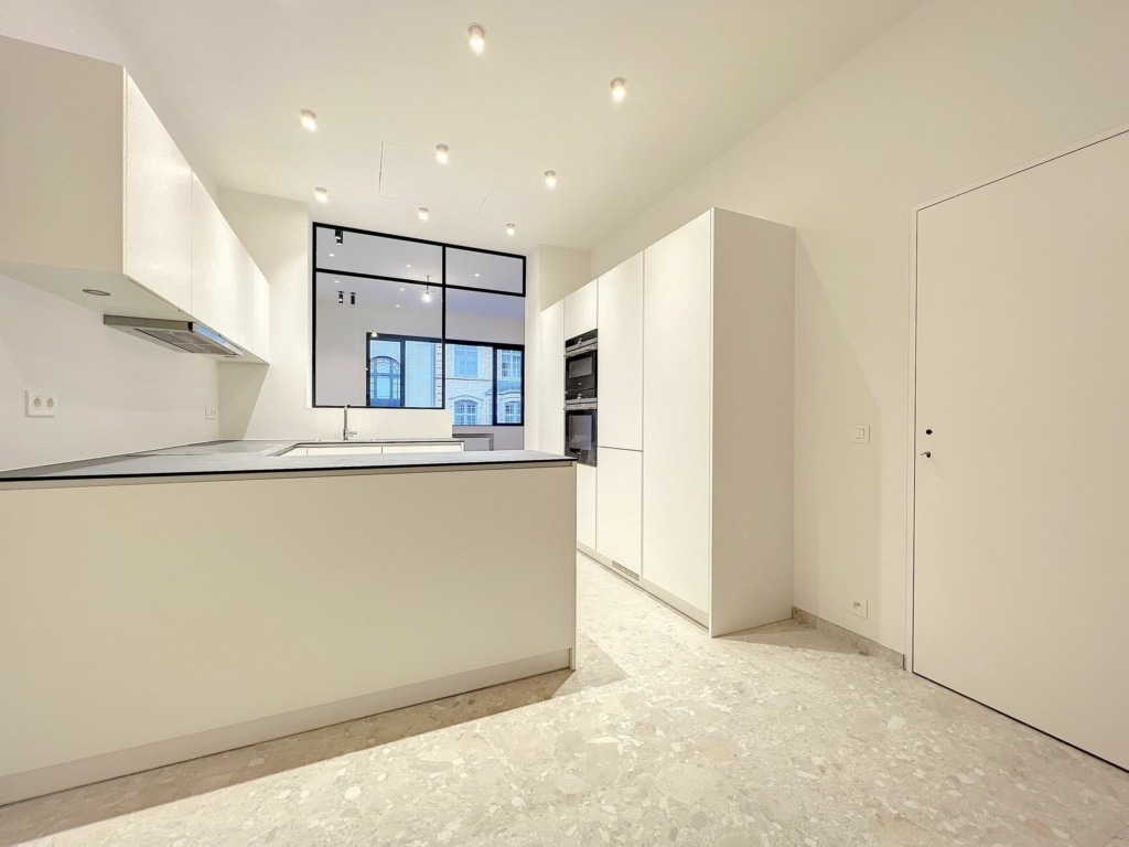 Cuisine contemporaine lumineuse, épurée avec îlot central, grande fenêtre et sol clair.
