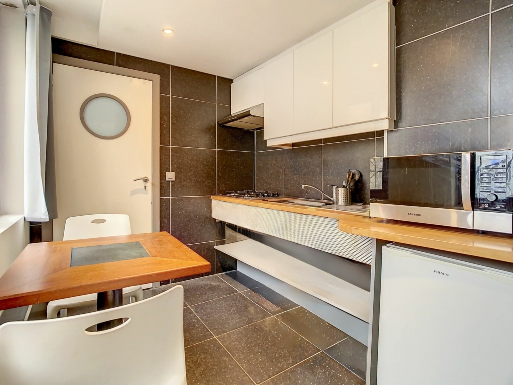 Cuisine moderne minimaliste avec murs gris, meubles blancs, accents en bois et éclairage élégant.