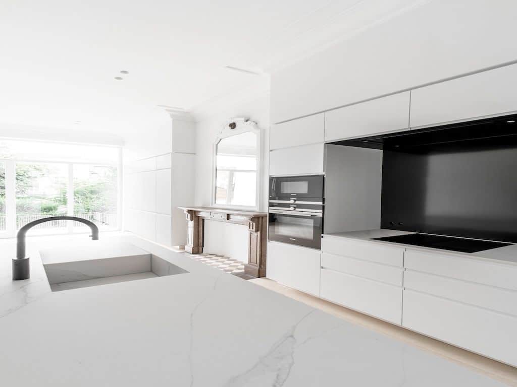 Cuisine moderne blanche minimaliste avec îlot en marbre et éclairage naturel, élégance et fonctionnalité.