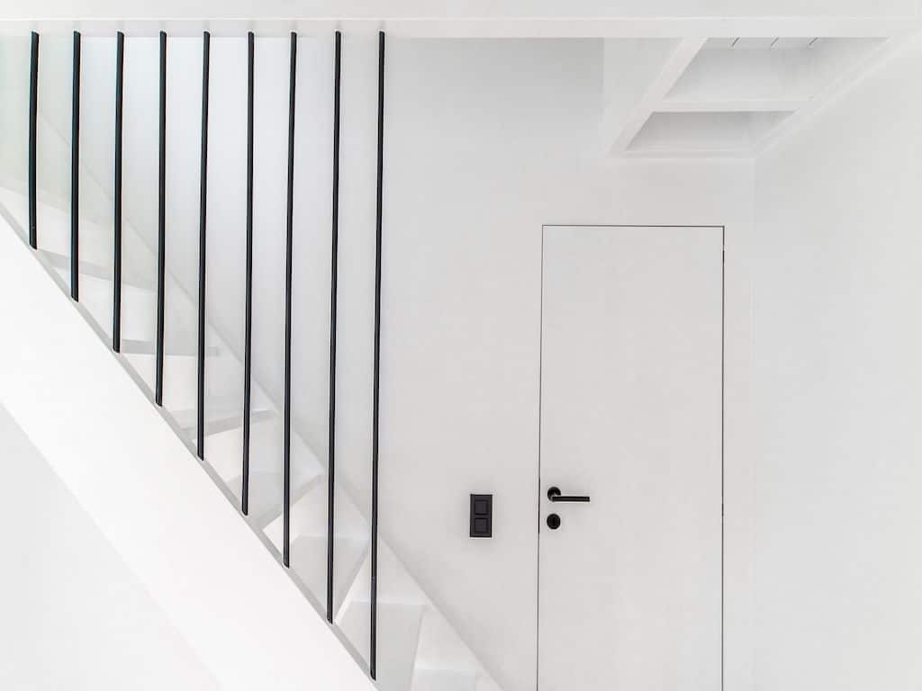 Escalier blanc moderne avec barres noires fines et éclairage naturel dans espace épuré.