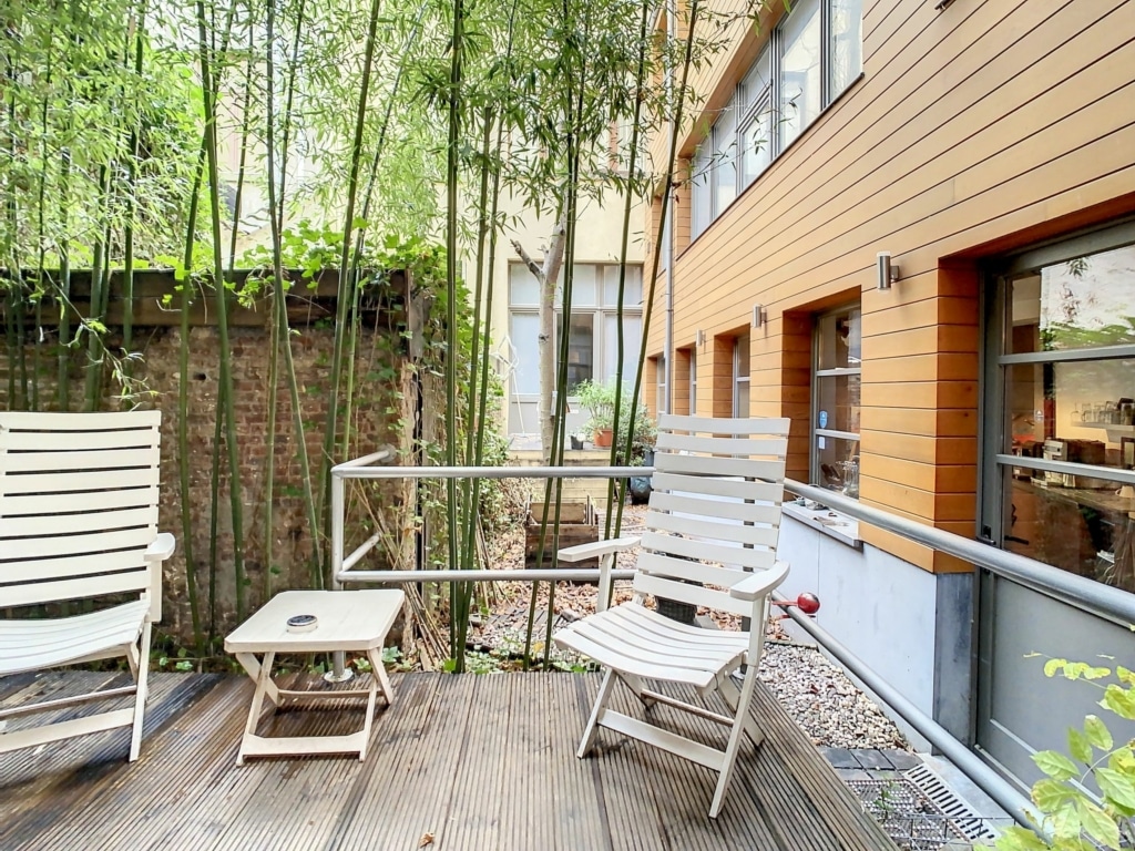 Coin extérieur zen avec chaises blanches, bambous verts, et façade en bois moderne.