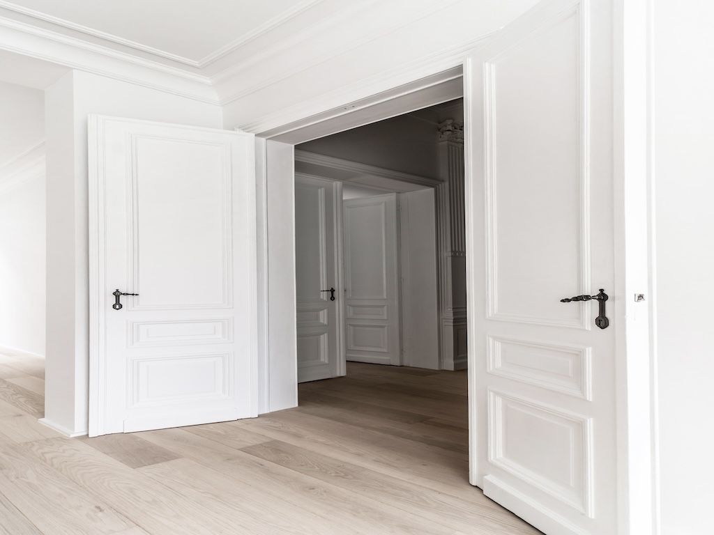 Intérieur moderne minimaliste avec portes blanches, parquet clair et lumière naturelle abondante.